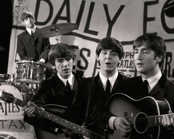 Les Beatles, le groupe le plus connu au monde, jouent sur scène. John Lennon et Paul McCartney chantent, George Harrison joue de la basse, Ringo Starr est à la batterie.