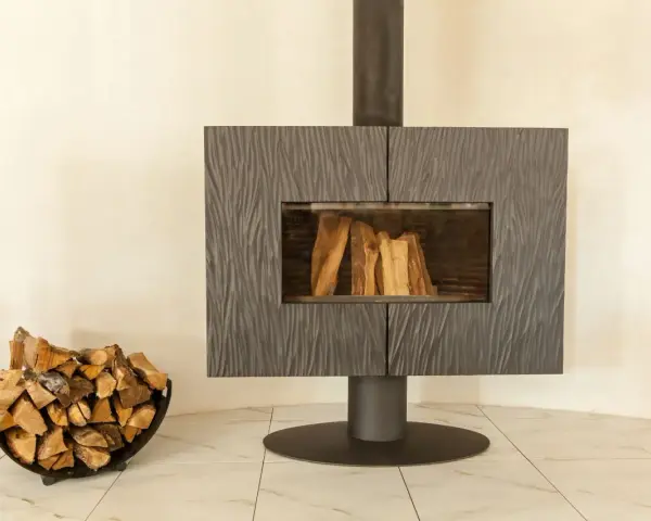 Un poêle moderne avec une cheminée vitrée et du bois de chauffage dans un panier. La **déco derrière un poêle** est sobre, mettant en valeur l'âtre.