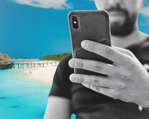 Mężczyzna z telefonem na plaży na Zanzibarze, sprawdzający zanzibar internet. W tle turkusowa woda i drewniany pomost.