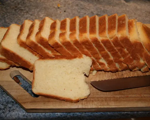 Tranches de pâte à pain de mie dorées et moelleuses, prêtes à être dégustées sur une planche en bois avec un couteau.