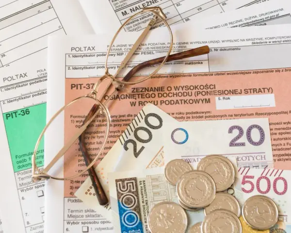 Okulary na dokumentach podatkowych PIT i pieniądzach. Zrozumienie, z czego wynika niedopłata podatku, wymaga analizy tych dokumentów.