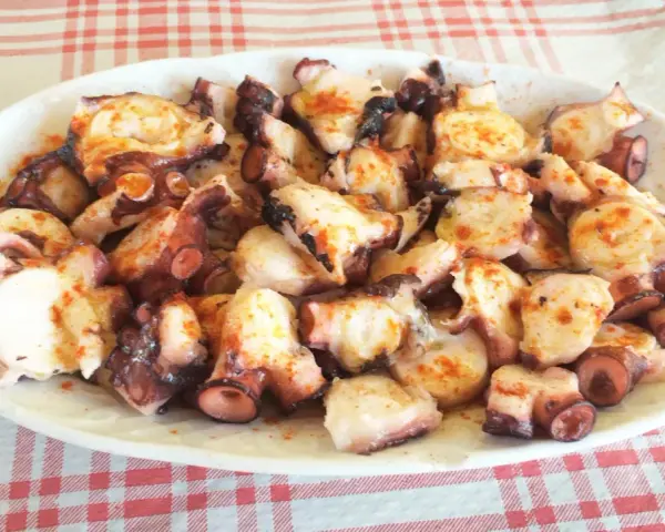 Pulpo a la gallega servido en plato blanco sobre mantel a cuadros rojos y blancos.