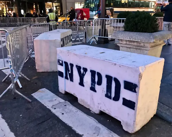 Betonowe bariery NYPD na ulicy. Czy w USA jest bezpiecznie? Widać ludzi i ruch uliczny w tle.