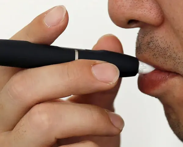 Persona usa un dispositivo IQOS. Las opiniones médicas sobre IQOS son variadas, pero este dispositivo calienta tabaco en lugar de quemarlo.