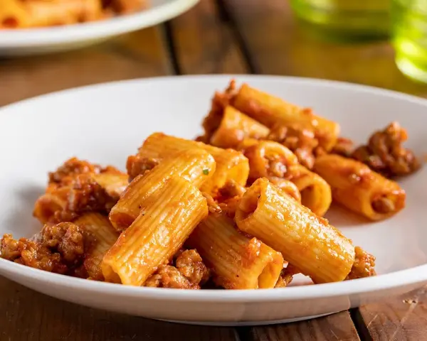 Rigatoni conditi con un ricco ragù di salsiccia, serviti su un piatto bianco.