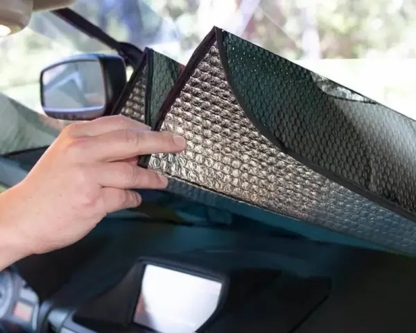Mani che posizionano un parasole riflettente sul cruscotto per proteggere l'auto dal sole.