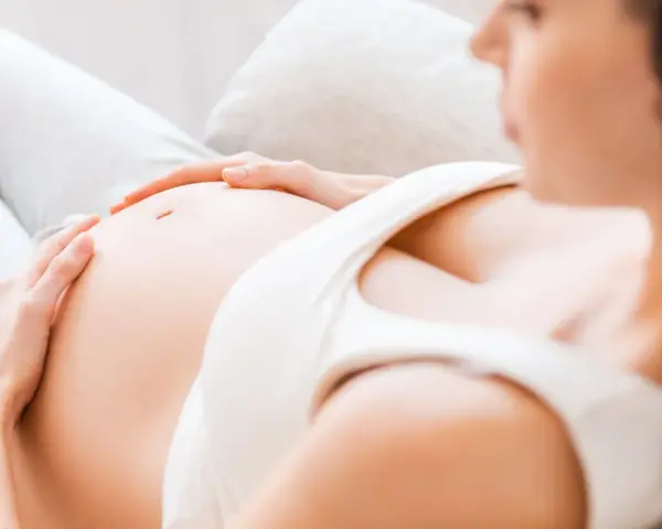 Kobieta w 7 miesiącu ciąży delikatnie głaszcze swój brzuszek.