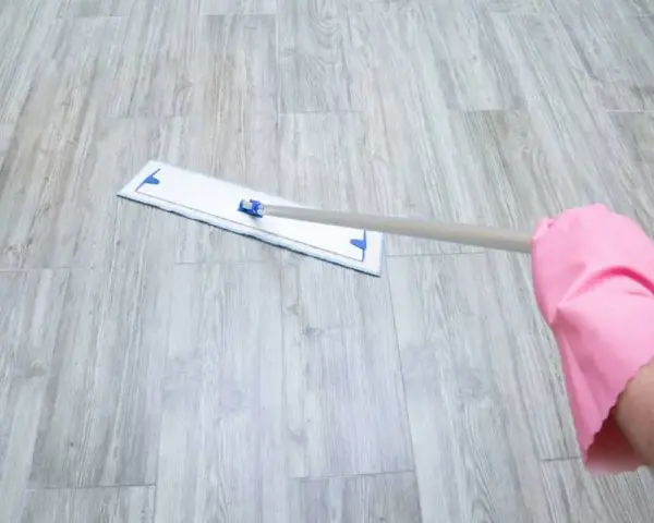 Mano con guante rosa limpiando suelo vinílico con mopa.