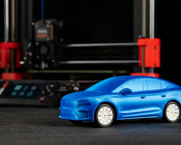 Niebieski model samochodu, gotowy do drukowania, stoi przed drukarką 3D.