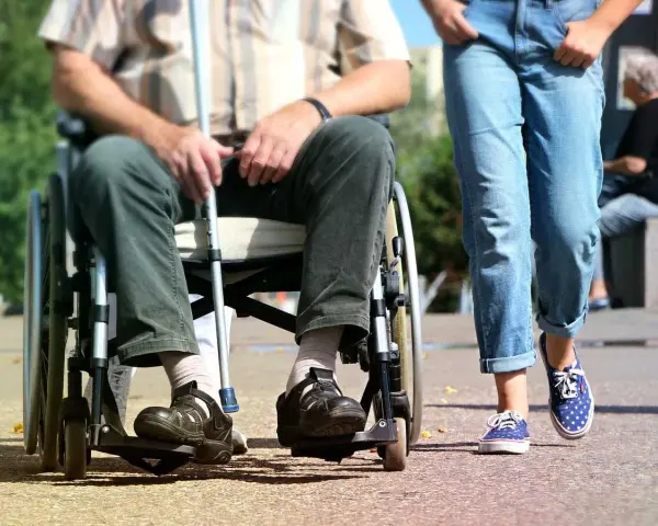 Osoba na wózku inwalidzkim z laską obok idącej osoby. Ulga na śmieci dla niepełnosprawnych to ważny temat.