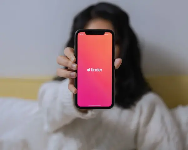 Osoba trzyma telefon z widocznym logo Tindera. Chcesz wiedzieć, jak sprawdzić, czy ktoś ma Tindera?