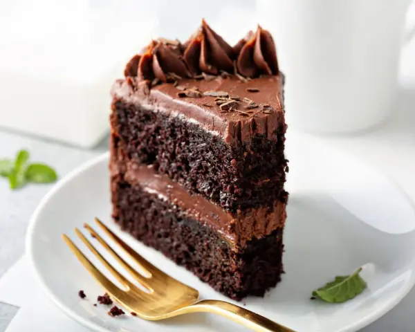 Rebanada de tarta de chocolate con glaseado cremoso y virutas de chocolate. Un tenedor dorado espera pacientemente para probar este delicioso postre.