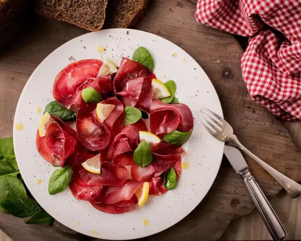 Bresaola affettata finemente, guarnita con spinacini freschi e spicchi di limone. Un'idea semplice su come condire la bresaola per un antipasto leggero.