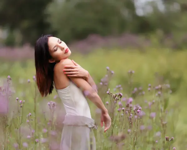 Portrait en bokeh d'une femme aux yeux fermés, bras croisés sur la poitrine, dans un champ de fleurs sauvages mauves.