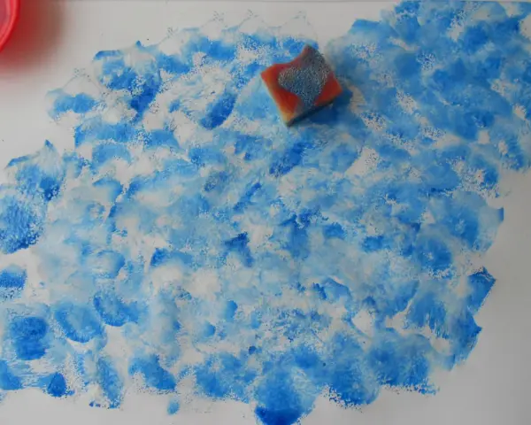 Peinture à l'éponge sur toile, créant un effet de vagues bleues et blanches. Une éponge est posée sur la toile.