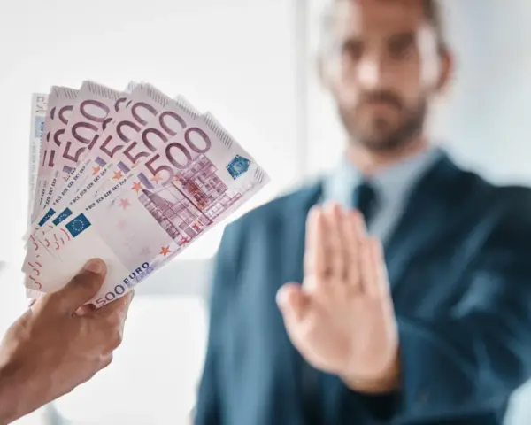 Ręka podaje plik banknotów 500 euro. Mężczyzna w garniturze odrzuca ofertę, mówiąc, że klient nie zapłacił za usługę.