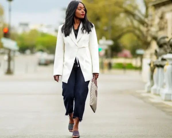 Mujer con un look smart elegant, lleva un blazer blanco, jeans oscuros y sandalias de diseño.
