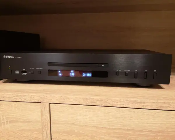 Czarny odtwarzacz CD Yamaha CD-S303 na drewnianej półce, gotowy do testu. Wyświetlacz pokazuje utwór 10 z 2:08.