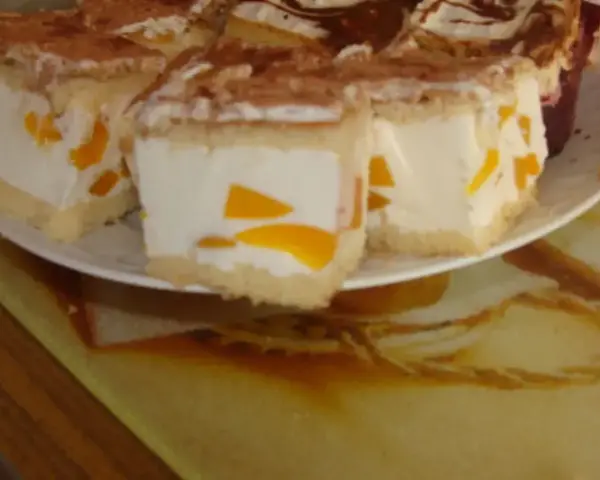 Sernik z bitą śmietaną siostry Anastazji, z kawałkami brzoskwini, posypany kakao. Pyszny deser na talerzu.