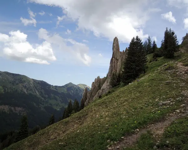 Ein steiler Bergpfad führt am markanten Siplinger Kopf vorbei, umgeben von grünen Hängen und Nadelbäumen.