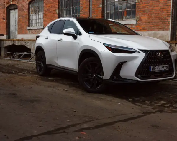 Biały Lexus 350h z czarnymi felgami stoi przed starą ceglaną budowką.