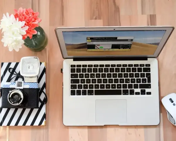 Jak zgrać zdjęcia z aparatu na laptop? Na biurku leży aparat, laptop i myszka.
