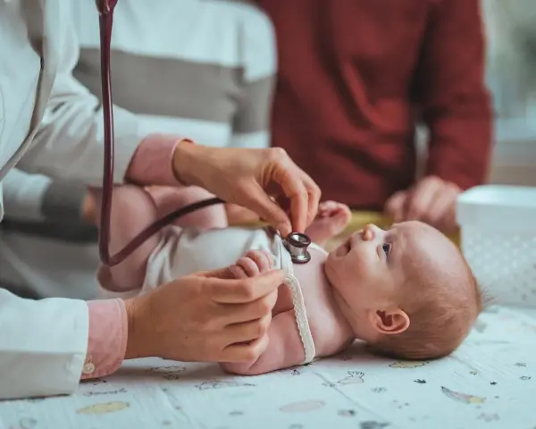Pielęgniarka środowiskowa po porodzie osłuchuje noworodka. Rodzice obserwują badanie.