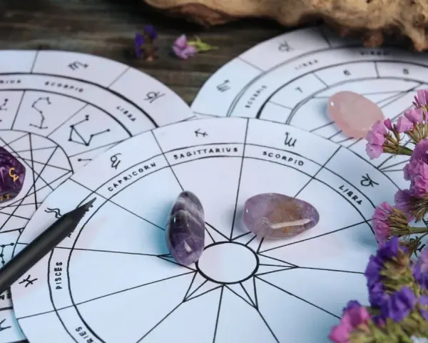 Astrologiczne koła zodiaku, kamienie, kostki i fioletowe kwiaty. 27 wrzesień znak zodiaku to Waga, symbolizująca równowagę.
