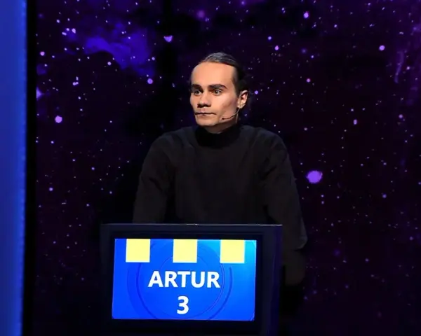 Artur, który wygrał jeden z dziesięciu, stoi na scenie w czarnym golfie.