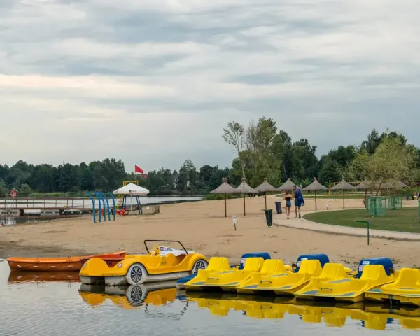 Żółte rowerki wodne i łódki czekają na plaży. Idealne miejsce na wypoczynek, jak na Mazurach blisko Warszawy.