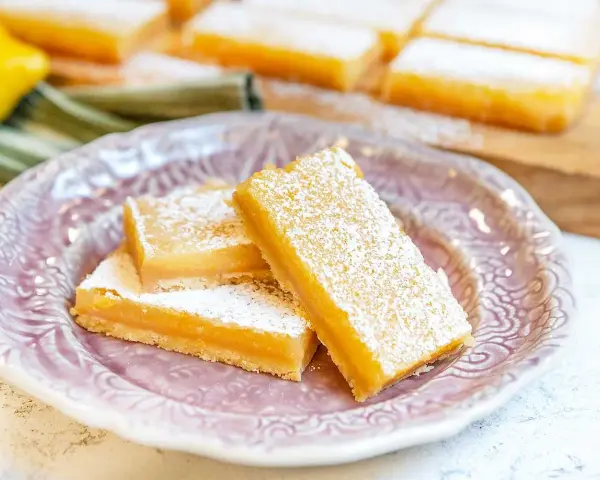 Citronkaka i långpanna, pudrad med florsocker, ligger upplagd på en vacker lila tallrik.