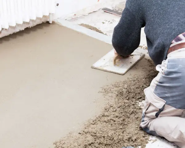 Operaio al lavoro con una cazzuola, livella il cemento per aumentare l'altezza del pavimento.