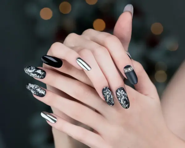 Mani con unghie particolari: nero lucido, argento specchiato e decorazioni floreali in bianco e argento con strass.
