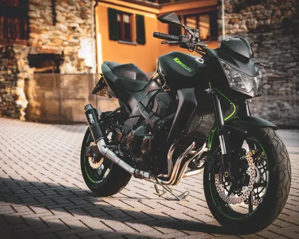 Czarny motocykl Kawasaki na brukowanej ulicy, z budynkami w tle.