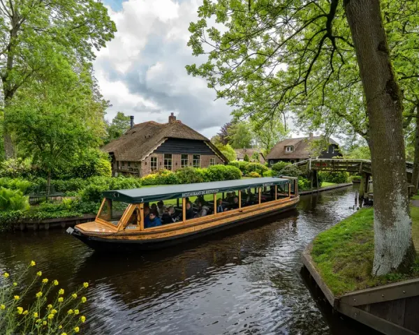 Bootfahrt durch Giethoorn, das Venedig der Niederlande. Grüne Ufer, Reetdachhäuser und gelbe Blumen am Wasser.