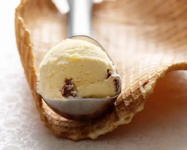 Ein Löffel cremiges Eis mit Rosinen und einem Hauch Rum ruht auf einem Waffelrand.