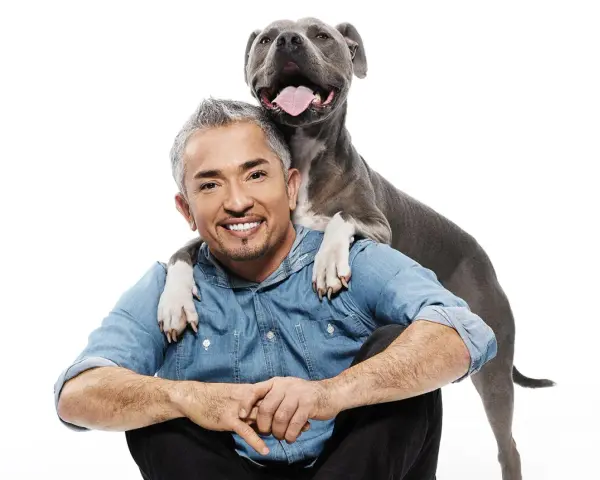 Cesar Millan z uśmiechniętym psem, który kładzie mu łapy na ramionach.