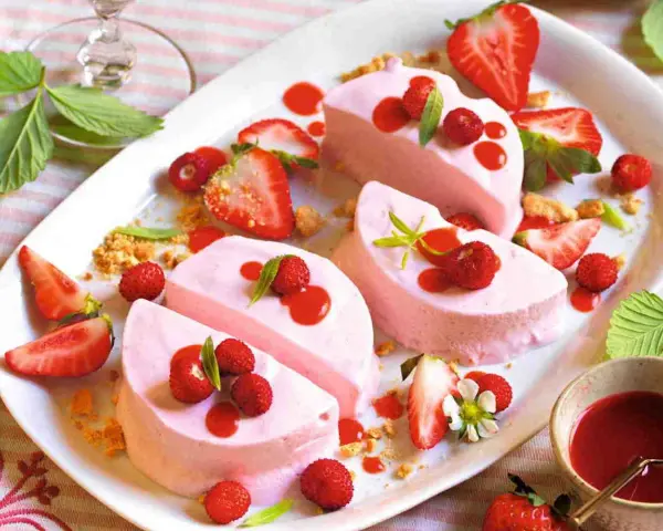 Delizioso semifreddo alle fragole, guarnito con fragoline di bosco, salsa rossa e foglioline verdi.