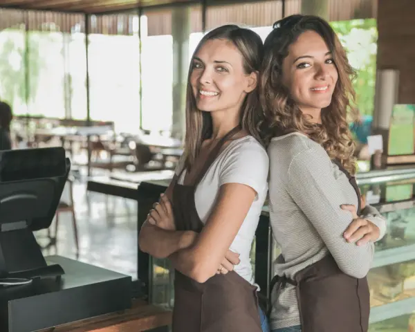 Dwie uśmiechnięte pracownice kawiarni, gotowe do obsługi. Od ilu lat można pracować w gastronomii? Odpowiedź znajdziesz w przepisach.
