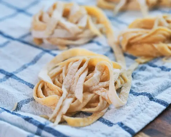 Świeże, domowe tagliatelle lub makaron spaghetti ułożone na lnianym ręczniku w kratkę.