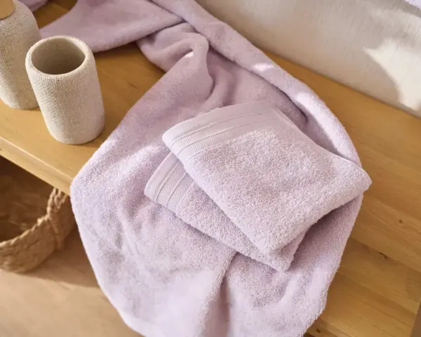 Variedad de tipos de toallas de baño en color lavanda, apiladas sobre una superficie de madera.