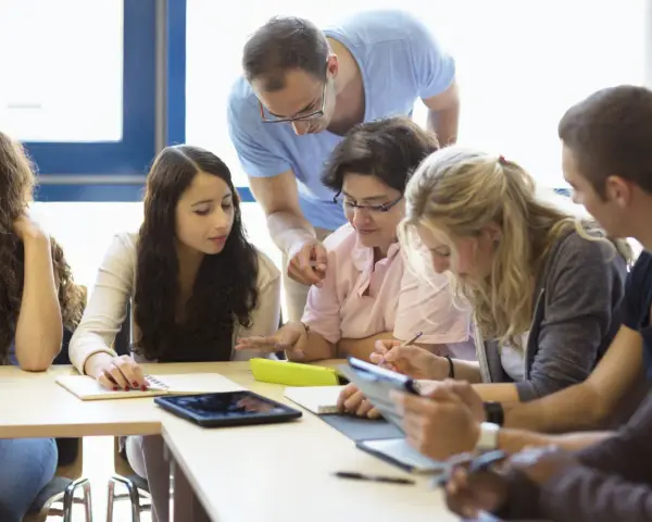 Des étudiants travaillent en groupe, un enseignant les supervise. Ils préparent leur diplôme BAFD, concentrés sur leurs notes et tablettes.