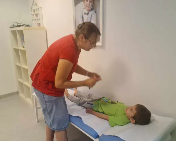 Lekarz bada chłopca leżącego na kozetce, oceniając objawy uszkodzonego układu nerwowego u dziecka.