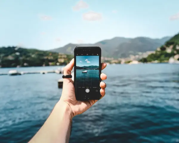 Dłoń trzyma smartfon, na ekranie którego widać zdjęcie jeziora z łódką. To przykład techniki photo stacking, która pozwala uzyskać niezwykłą głębię ostrości.