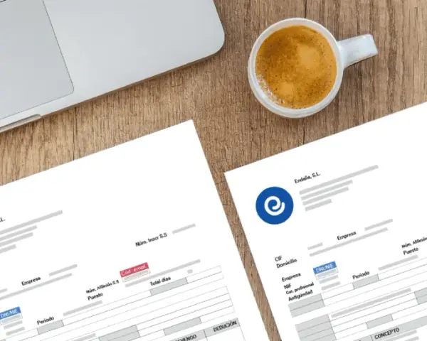 Documentos de nómina listos para ser procesados con un programa para hacer nominas. Café y portátil sugieren un entorno de trabajo.