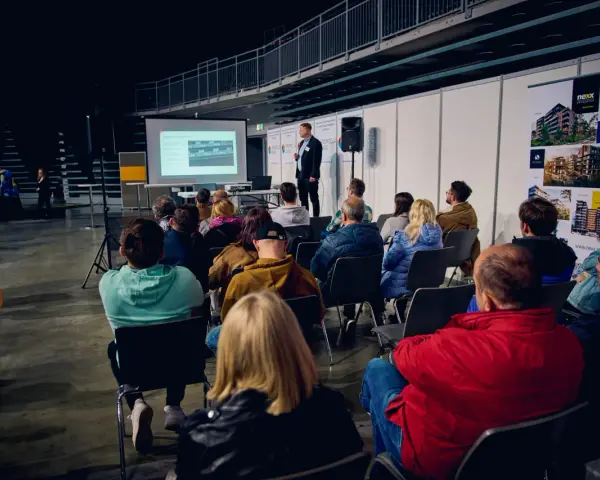 Prezentacja na targach budowlanych. Mężczyzna przemawia do zgromadzonej publiczności, która siedzi na krzesłach.