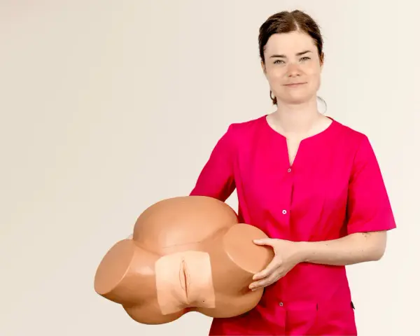 Kobieta w różowej bluzce prezentuje model miednicy do nauki masażu krocza przed porodem.