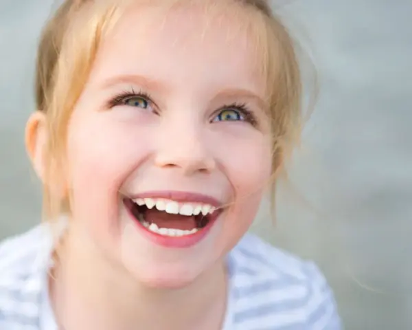 Uśmiechnięta dziewczynka z blond włosami, której radość przypomina o sile ducha w walce z zespołem Angelmana.