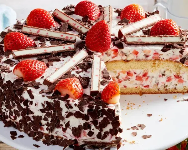 Eine köstliche Yogurette Torte mit frischen Erdbeeren, Schokostückchen und Sahne. Ein Stück ist bereits angeschnitten.