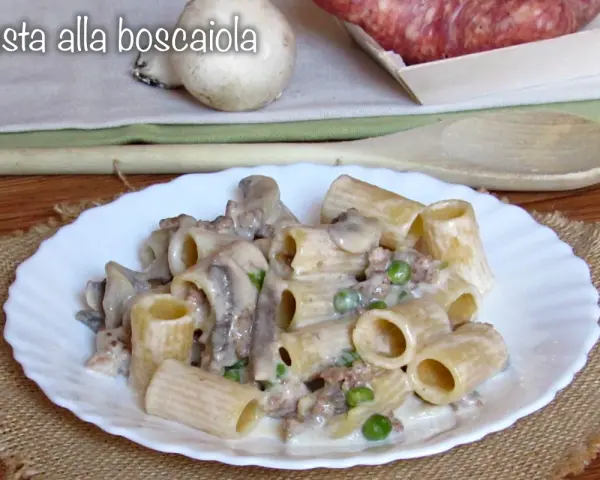 Piatto di pasta alla boscaiola con funghi, piselli e salsiccia, servita su un piatto bianco con una tovaglietta di juta.